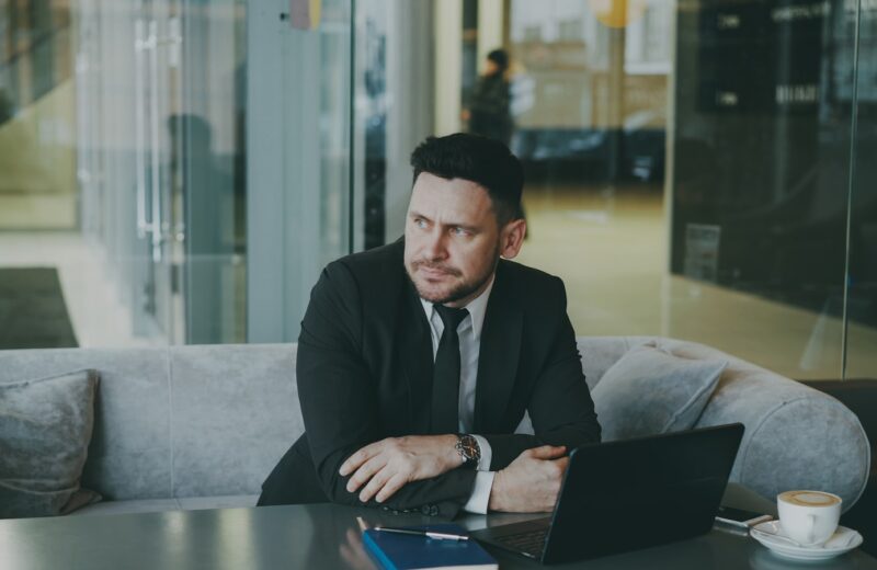 Man in suit sitting at table with laptop and coffee.