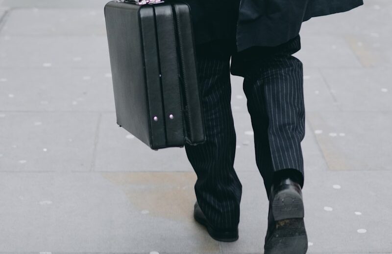 person carrying suit case while walking on pavement