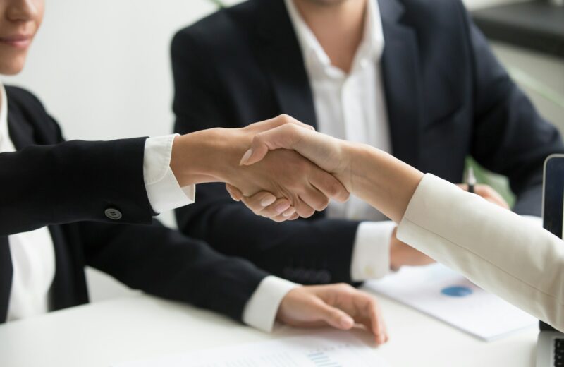 two people shaking hands in front of a laptop